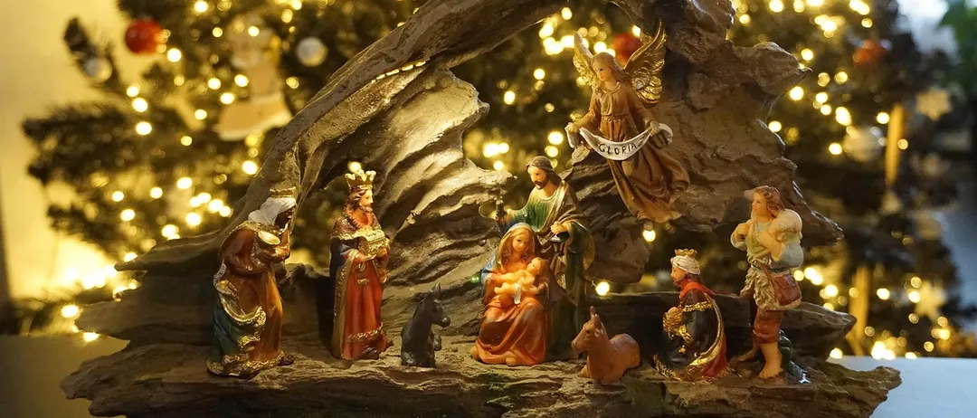 Vor einem Weihnachtsbaum ist eine Krippe aufgestellt. Die Szene zeigt Maria, Josef, das Baby Jesus, einen Engel und die drei Weisen. Der Hintergrund ist unscharf und hebt die Krippe hervor.