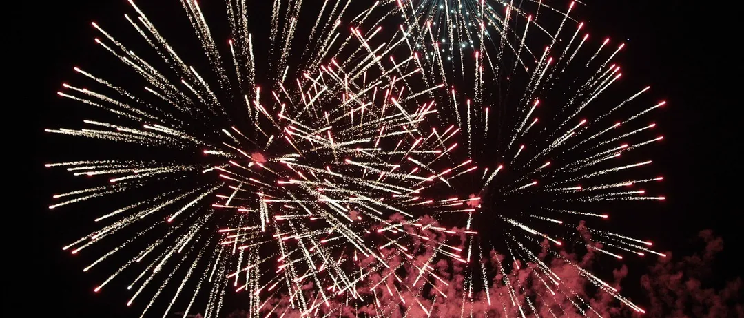 Ein Nachthimmel ist mit leuchtenden Feuerwerken gefüllt und zeigt eine Vielzahl von Farben, darunter Rot, Weiß und Blau. Die Feuerwerke explodieren in verschiedene Richtungen und erzeugen ein spektakuläres Display.
