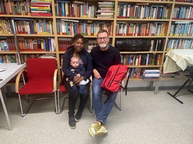Eine Familie sitzt in einer Bibliothek. Ein Mann und eine Frau halten ein Baby. Sie sind von Bücherregalen umgeben.