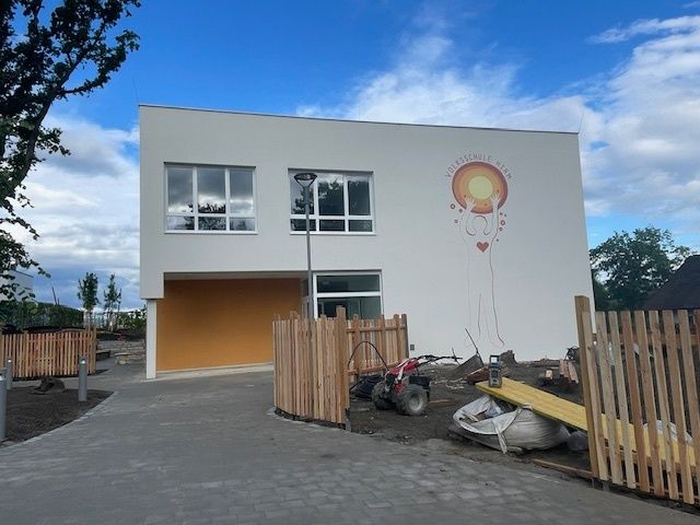 Ein weißes Gebäude mit Glasfenstern, einer Garage und einem Wandbild. Der Bereich davor ist im Bau.