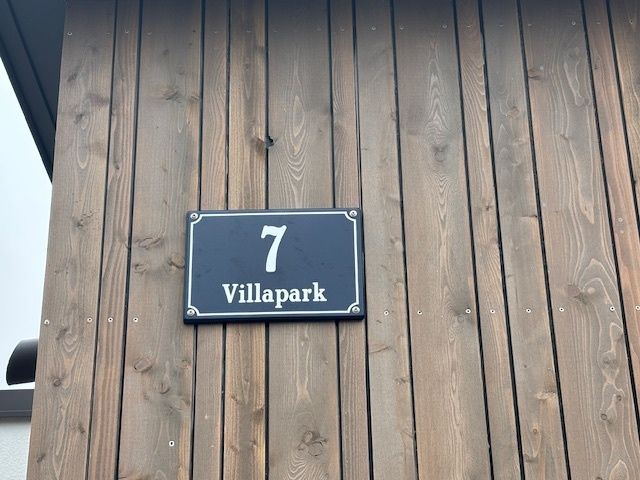 Eine Holzwand hat ein blaues Schild mit weißem Text und der Nummer 7. Unter der Nummer steht das Wort Villapark.