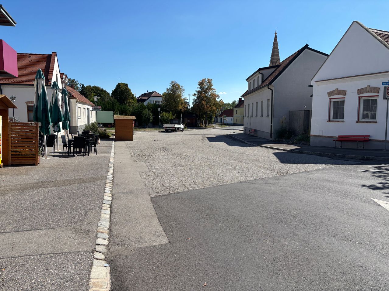 Eine leere Straße mit einem geparkten Lastwagen und Tischen für das Essen im Freien unter Schirmen. Im Hintergrund sind Gebäude und Bäume zu sehen.