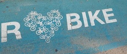 Eine blaue Straßenmarkierung mit einem Herzform-Fahrraddesign und dem Wort 'BIKE' in weißer Schrift. Die Buchstaben 'R' sind ebenfalls in weißer Schrift.
