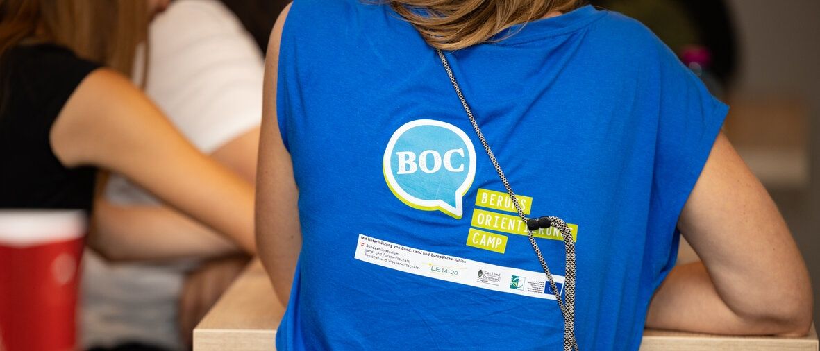 Eine Frau in einem blauen T-Shirt mit dem Text BOC sitzt in einem Raum.