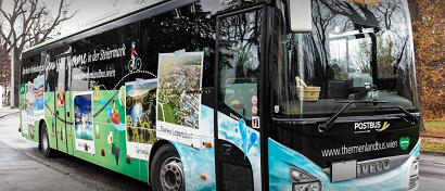 Ein Bus mit lebhaftem Design, das Bilder von Menschen und Bäumen enthält, parkt am Straßenrand. Der Bus hat vorne das Wort 'Postbus' und hinten 'VELOX' auf der Stoßstange.