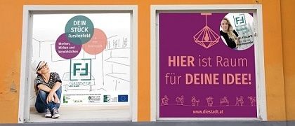 Ein orangefarbenes Gebäude mit zwei Glasfenstern zeigt eine Frau, die auf dem Boden sitzt. Die Fenster zeigen ein Plakat mit dem Text 'Hier ist Raum für deine Idee!' und einem Bild einer Frau. Das Plakat enthält auch Logos und die Website-Adresse 'www.diestadt.at'.