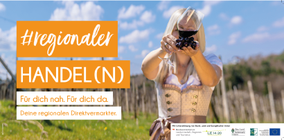Eine blonde Frau in einem traditionellen bayerischen Kleid hält ein Weinglas mit roter Flüssigkeit in einem Weinberg. Der Textüberlagerung lautet 'Regionaler Handel (N)' und 'Für dich. Für hier.' Das Bild zeigt auch Logos von Organisationen und der Europäischen Union.