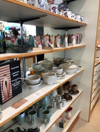 Ein Holzregal, das eine Vielzahl von Keramiktellern, -schüsseln und -bechern präsentiert. Links steht ein Buch mit dem Titel 'Keramik' von Lawrence Brazier.