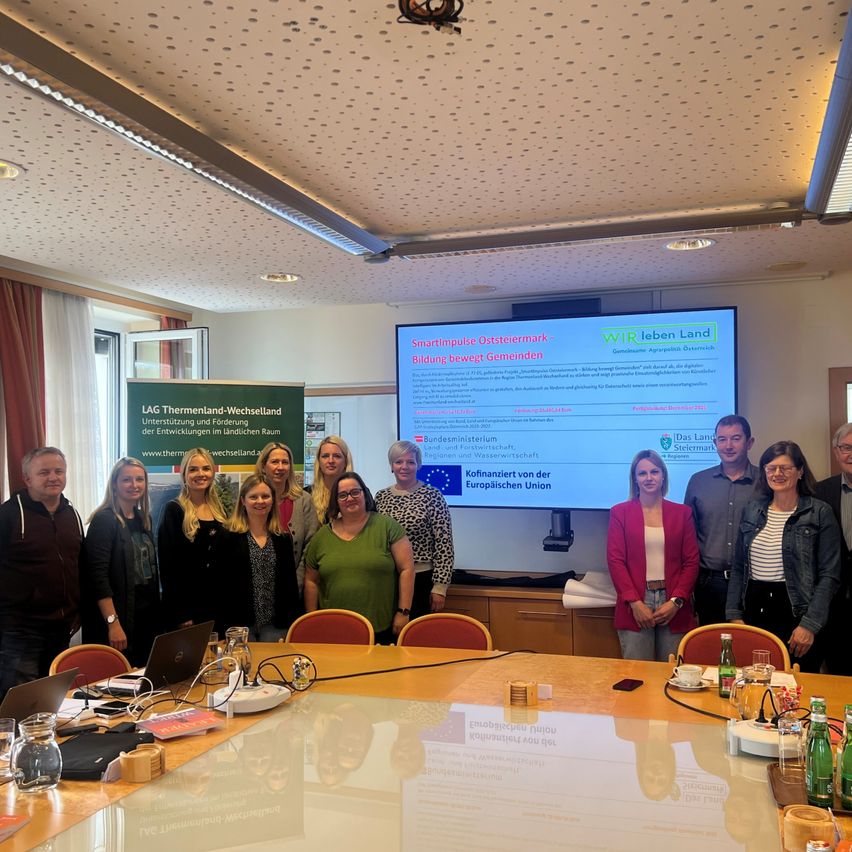 Eine Gruppe von Menschen, möglicherweise aus einem Workshop, steht vor einer großen Leinwand. Sie scheinen für ein Foto zu posieren, mit einer Präsentation im Hintergrund.