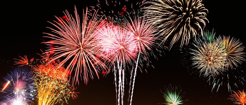 Eine leuchtende Feuerwerksshow explodiert in der Nacht, mit mehreren roten, gelben und grünen Lichtern, die die Dunkelheit erhellen.