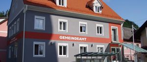 Das Bild zeigt ein Rathaus mit rotem Dach und roter Streifen, weißen Fenstern und einem Fahrrad, das davor geparkt ist.