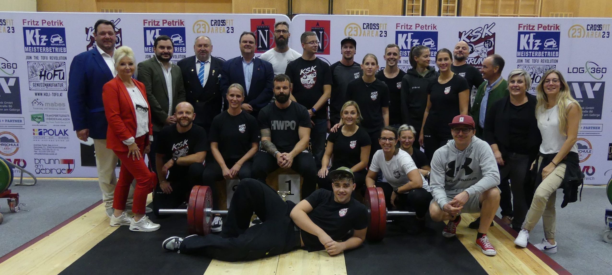 Gruppe von Menschen in schwarzen und weißen Shirts posiert mit Hanteln bei einer CrossFit-Veranstaltung.