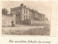 Eine Person steht vor einem beschädigten Gebäude im April 1945. Das Bild zeigt die durch den Krieg verursachte Zerstörung.