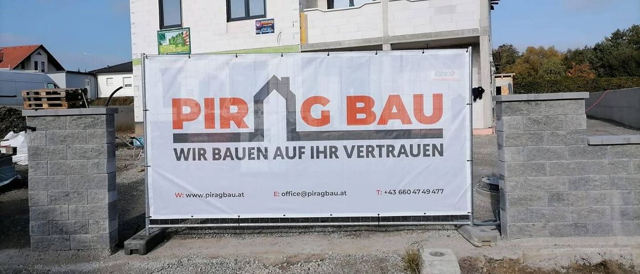 Ein großes weißes Banner mit rotem Text bewirbt Pir G Bau, ein Bauunternehmen, vor einem Gebäude. Das Banner enthält die Website und Kontaktnummer des Unternehmens.