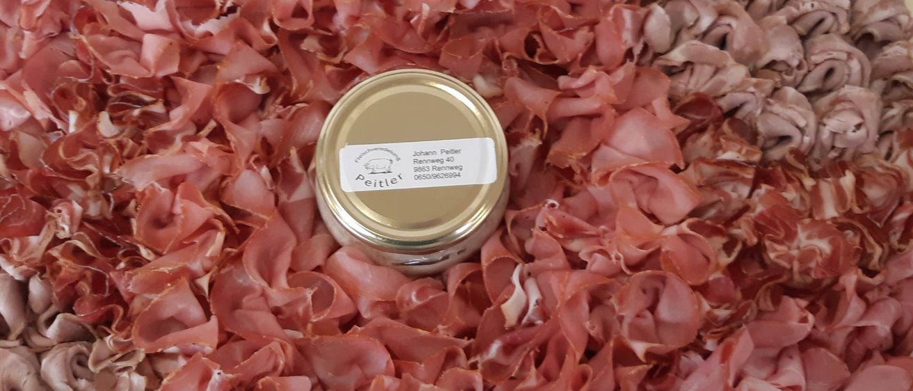 Ein Glas mit einem Deckel auf einem großen Haufen geschnittenem Schinken, alles in Plastik verpackt.