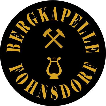 Ein rundes Logo mit 'Bergkapelle' und 'Johannsdor' in Gold auf schwarzem Hintergrund, mit einem Leier- und Spitzhackensymbol.