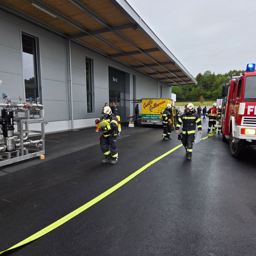 Firefighters in uniform are practicing at the fire station. A fire truck is parked next to the building.
