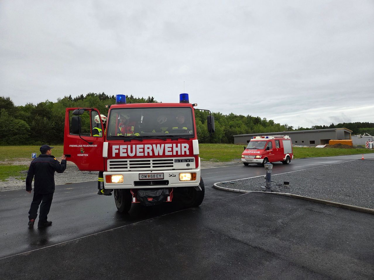 A red fire truck with the word Feuerwehr on the front, parked on a road with another fire truck in the background.