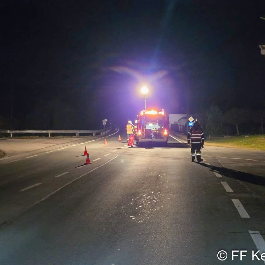 At night, emergency workers are on the road. A fire truck is parked, and traffic cones are placed. A person in a reflective vest walks towards the truck.