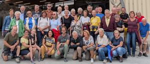 Eine Gruppe von Menschen posiert für ein Foto vor einem Gebäude mit einem Schild, das 'STYROMAG' steht. Das Gebäude hat Glasfenster und einen großen offenen Eingang.