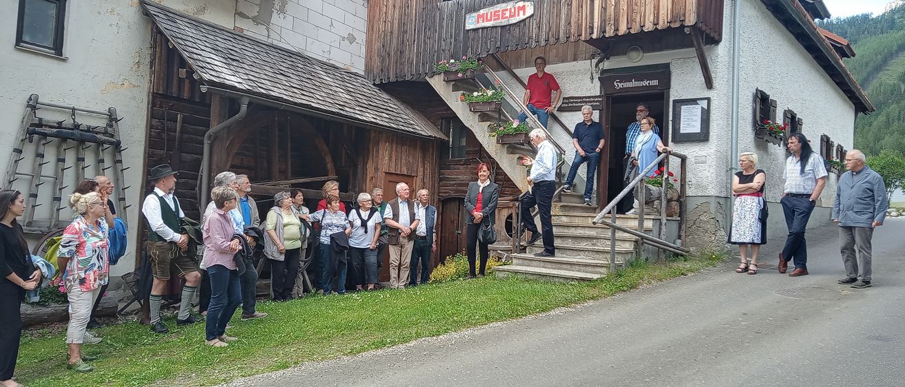 Eine Gruppe von Menschen steht vor einem Holzgebäude mit dem Schild Museum. Sie sind wahrscheinlich Touristen. Einige betrachten die Blumen.