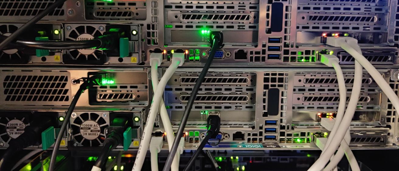 Ein Nahaufnahme eines Server-Racks mit mehreren Kabeln angeschlossen. Grüne LEDs zeigen Aktivität an der Vorderseite der Server an.