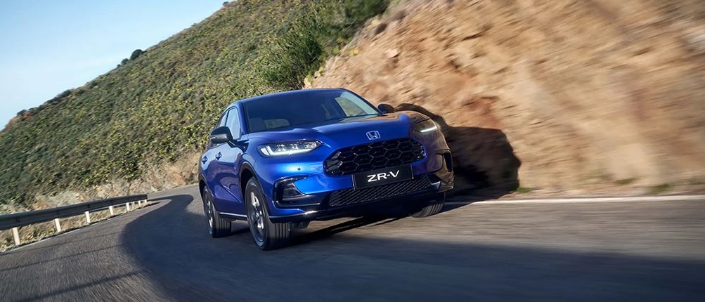 Ein blauer Honda ZR-V SUV fährt auf einer kurvenreichen Straße mit einem felsigen Hügel im Hintergrund.