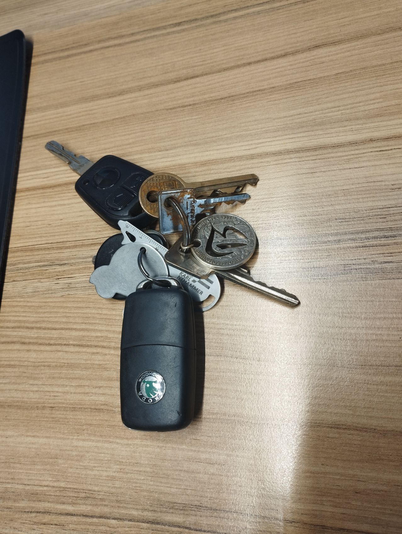 Verschiedene Schlüssel auf einem Holztisch, einschließlich eines Skoda-Schlüsselanhängers, sehen abgenutzt und alt aus.