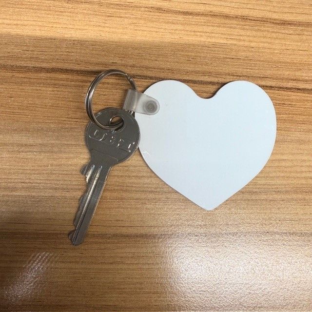 Ein silberner Schlüssel mit den Buchstaben UBER darauf ist an einem herzförmigen weißen Schlüsselanhänger auf einer Holzoberfläche befestigt.
