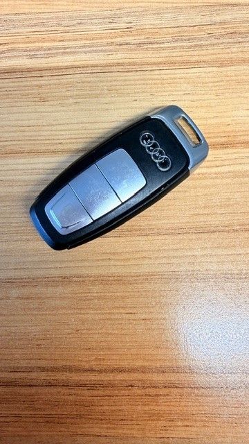 Ein schwarzer und silberner Audi-Fernbedienungsschlüssel mit vier Tasten liegt auf einer Holzoberfläche.