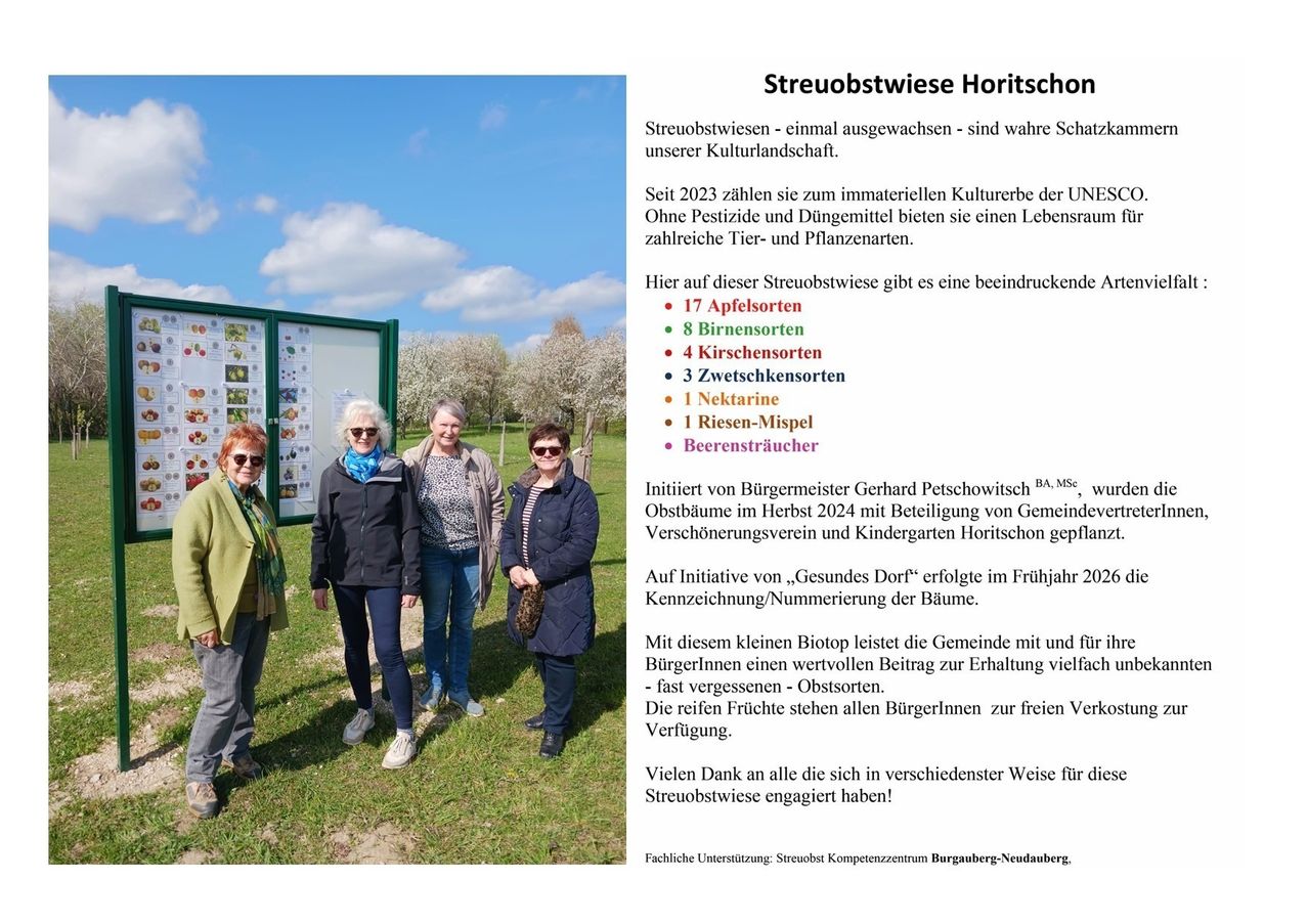 Vier Frauen stehen auf einem Grasfeld und posieren für ein Foto. Hinter ihnen steht ein grünes Schild mit verschiedenen Obst- und Gemüsesorten. Sie tragen Sonnenbrillen und Jacken. Die Initiative des Bürgermeisters ist auf dem Schild zu sehen. Der Text handelt von Streuobstwiese Horitschon, einem Naturerbe-Standort.