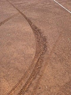 An aerial view of a dirt track with a white line and tire marks. The ground is brown.