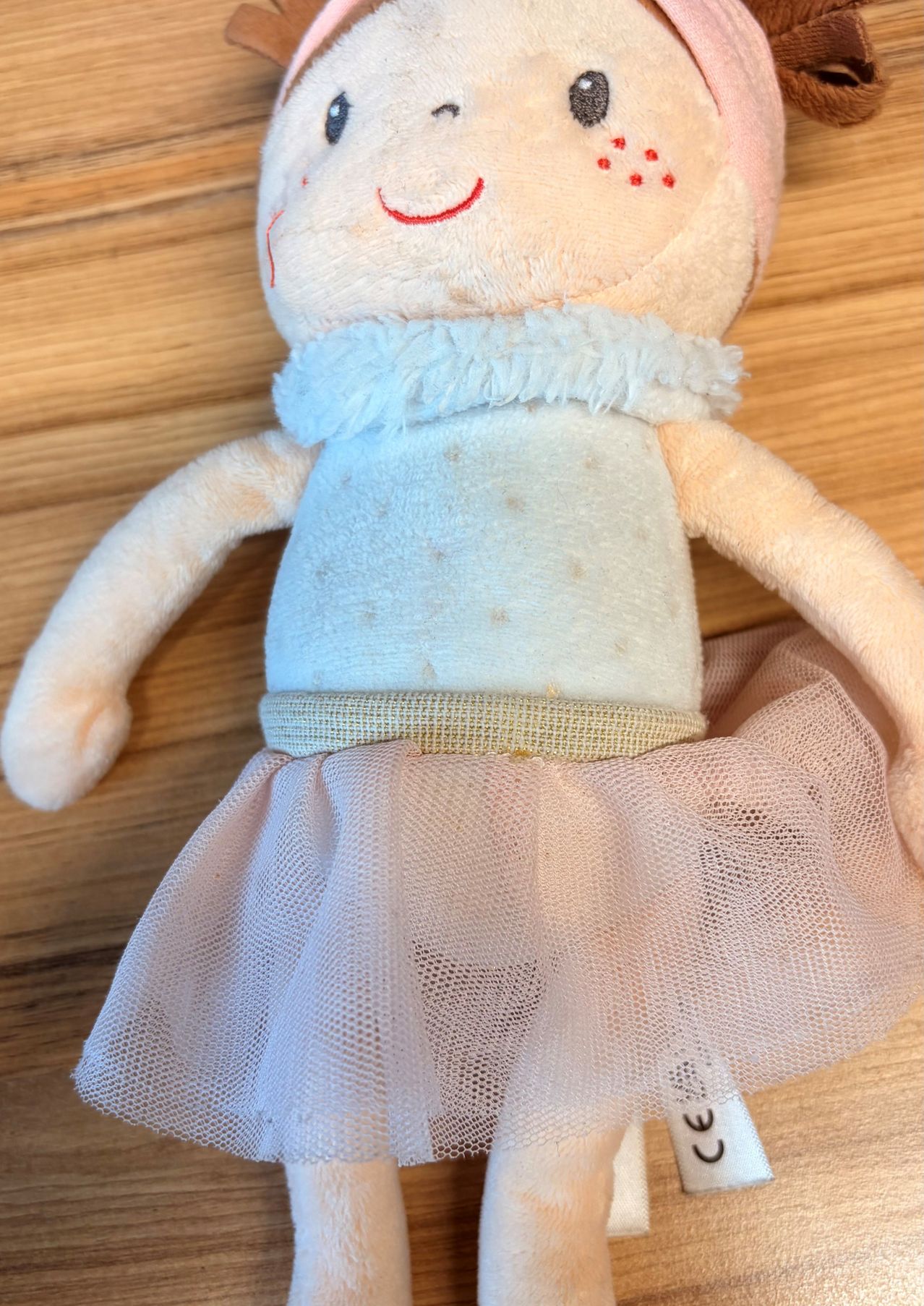Eine Stoffpuppe mit einem blauen Kleid und einem rosa Tüllrock liegt auf einer Holzoberfläche.