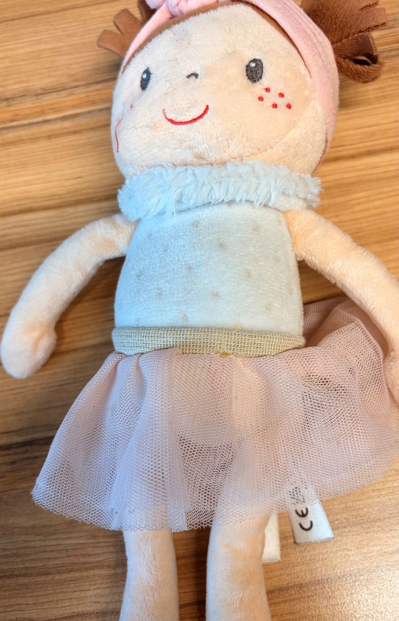 A stuffed doll with a blue dress and a pink tulle skirt is placed on a wooden surface.