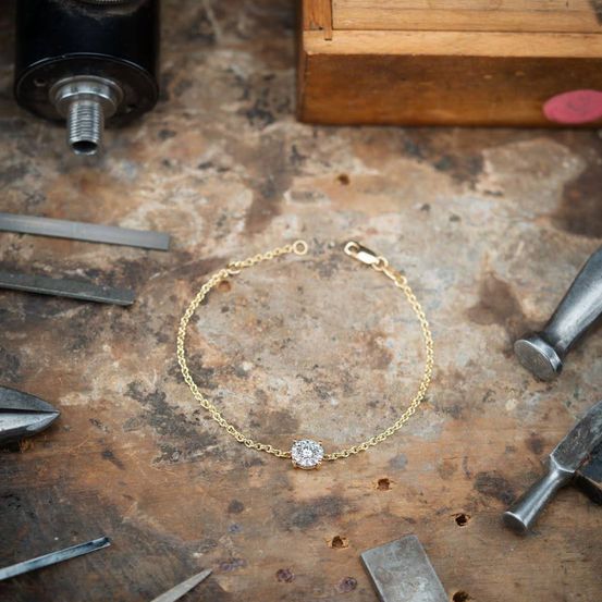 Ein goldenes Armband mit einem Diamanten liegt auf einem Werktisch. Verschiedene Werkzeuge wie Hämmer und Zangen sind darum herum.