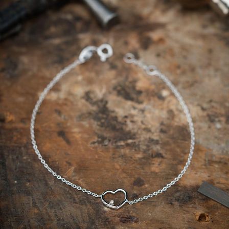 Ein silbernes Armband mit Herzanhänger liegt auf einer Holzoberfläche. Der Herzanhänger hat einen kleinen Diamanten in der Mitte.