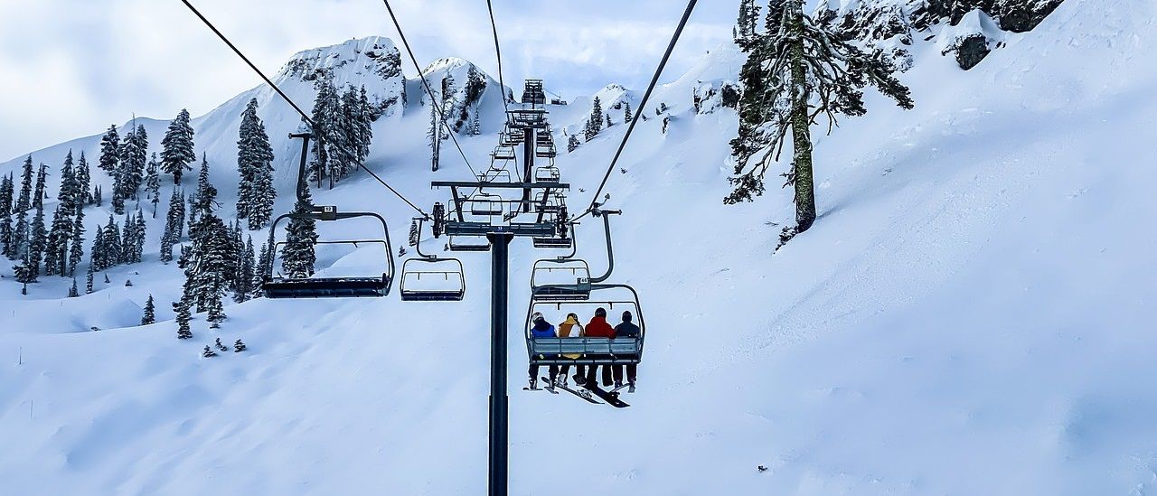 Eine Gruppe von Menschen auf einer Skilift, in Winterkleidung und hält sich an den Haltestangen des Lifts fest.
