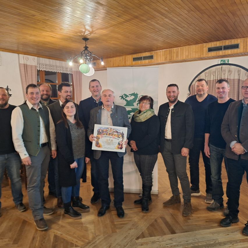 Eine Gruppe von Menschen steht in einem Raum und hält ein Zertifikat. Sie lächeln und schauen in die Kamera. Der Raum hat Holzböden und Wände.