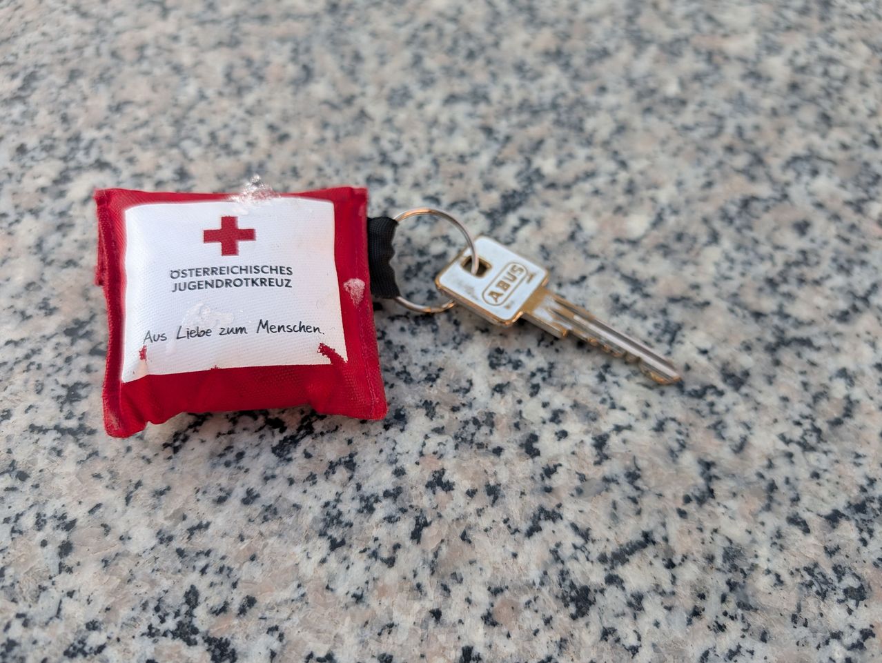 Ein rotes Erste-Hilfe-Set und ein silberner Schlüssel auf einer Granitoberfläche. Das Erste-Hilfe-Set hat ein rotes Kreuz auf weißem Hintergrund.