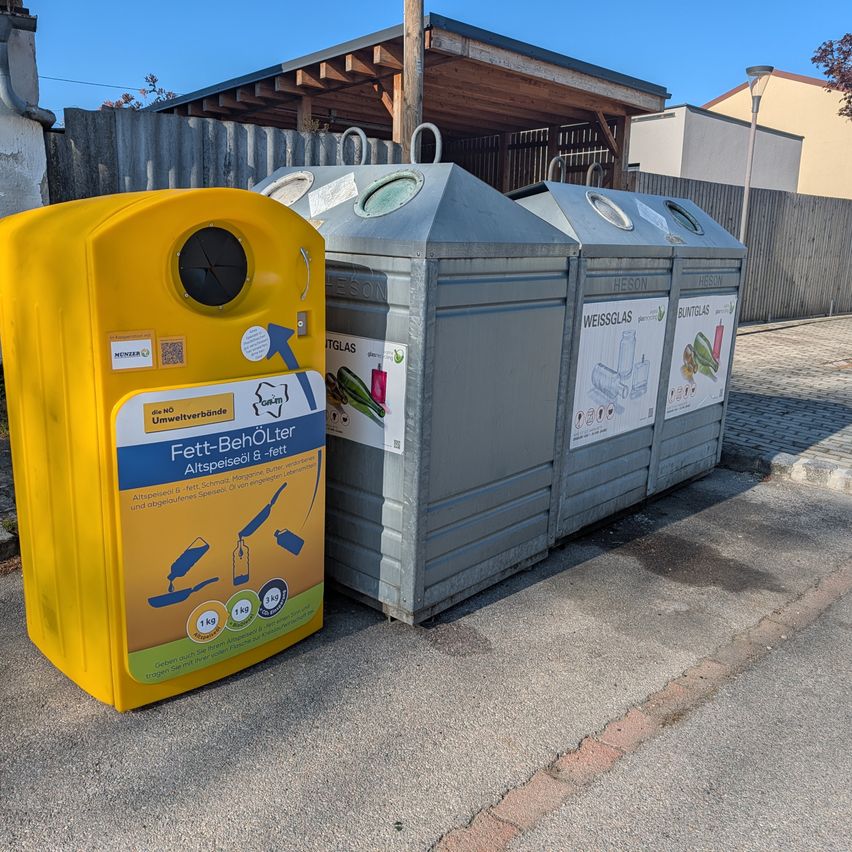 Drei Müllcontainer stehen am Straßenrand. Der gelbe ist für Fett, Öl und Fette. Die anderen beiden sind für weißes Glas und braunes Glas.