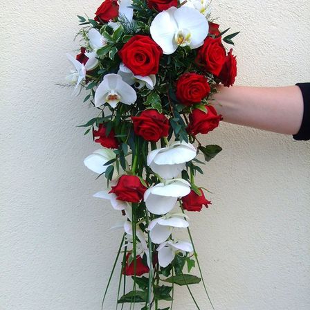 Ein Strauß aus weißen und roten Blumen, einschließlich Orchideen, von einer Hand gegen eine helle Wand gehalten.