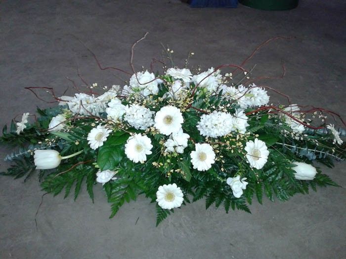 Ein Arrangement aus weißen Blumen und grünen Blättern liegt auf einer grauen Oberfläche. Die Blumen sind Tulpen und Gänseblümchen.