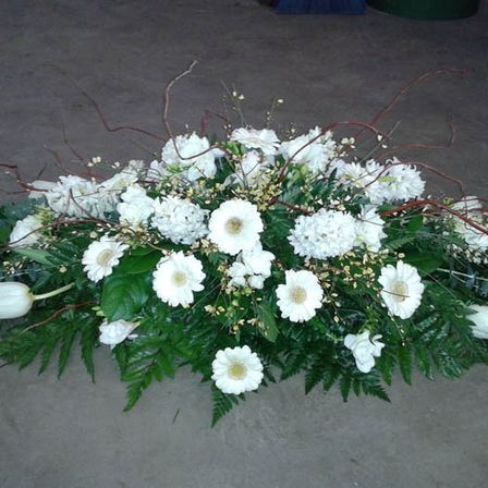Ein Arrangement aus weißen Blumen und grünen Blättern liegt auf einer grauen Oberfläche. Die Blumen sind Tulpen und Gänseblümchen.