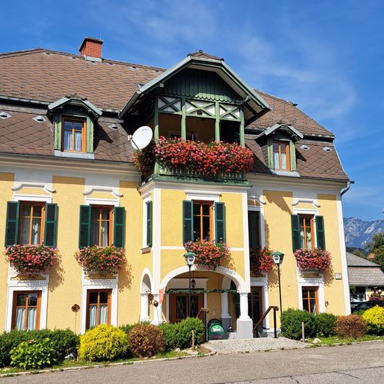 Ein gelbes Gebäude mit grünen Fensterläden und Balkonen, geschmückt mit roten Blumen unter einem klaren blauen Himmel.