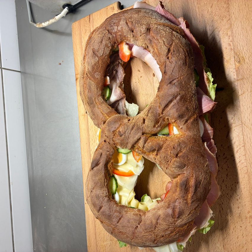Ein Sandwich in Form der Zahl 8 auf einem Holzbrett mit verschiedenen Zutaten im Inneren sichtbar.