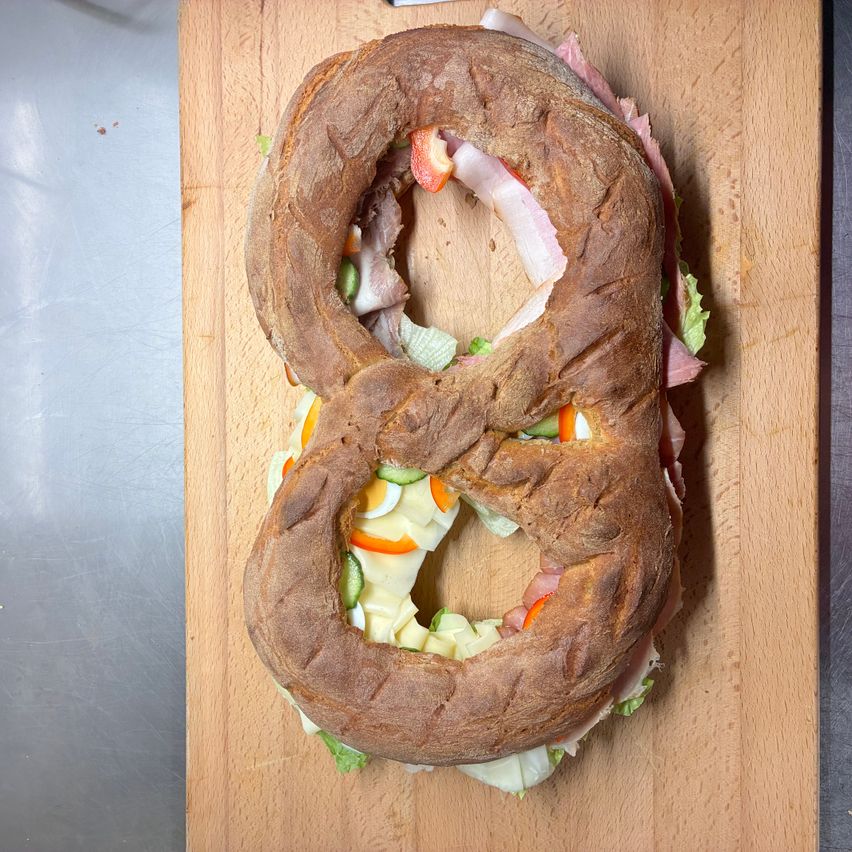 Ein Sandwich in Form der Zahl acht auf einem Holzschneidebrett, gefüllt mit Fleisch, Gemüse und Eiern.