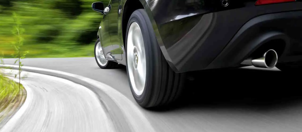 Ein schwarzes Auto fährt auf einer Straße mit einem verschwommenen Hintergrund aus grünen Bäumen.