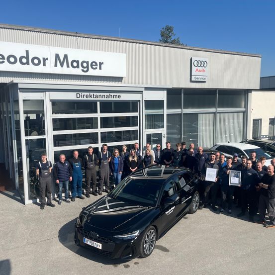 Eine Gruppe von Menschen in Uniformen steht vor einem Audi-Händler und posiert für ein Foto mit einem schwarzen Audi-Auto im Vordergrund.