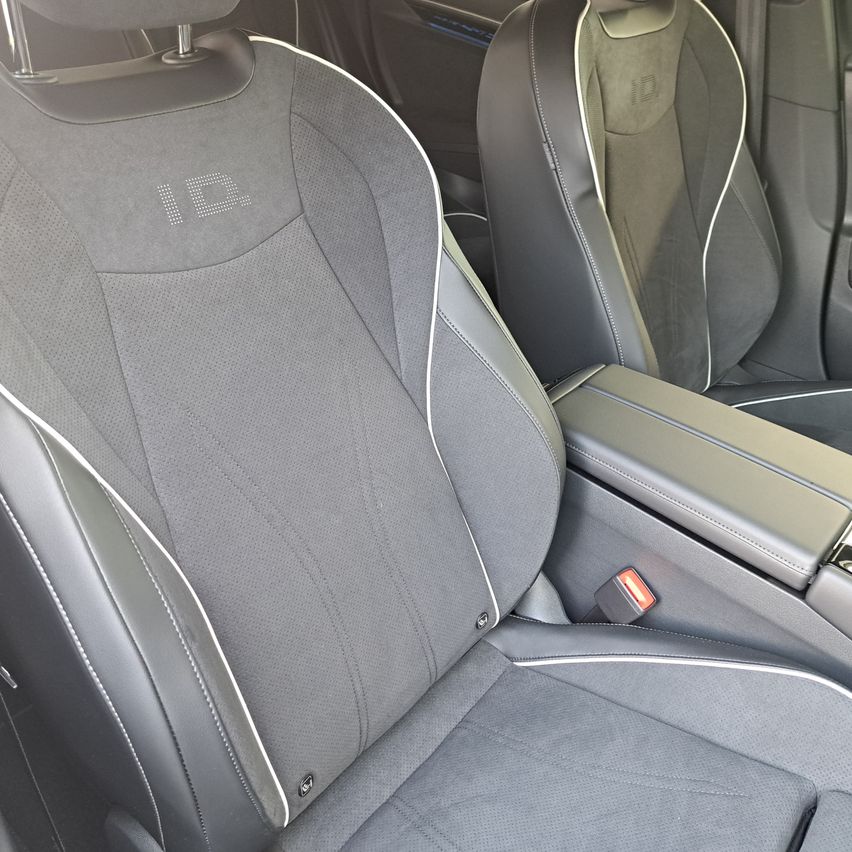 Das Innere eines Autos mit grauen Ledersitzen, aus Sicht des Fahrers. Der Vordersitz hat ein weißes ID-Logo darauf. Die Mittelkonsole enthält einen Sicherheitsgurtverschluss.