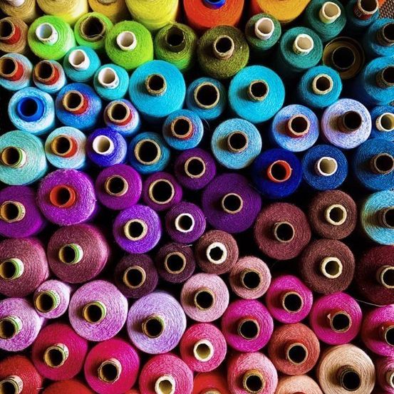 Eine bunte Auswahl an Spulen mit Garn in verschiedenen Größen und Farben, in einem Kreismuster angeordnet.